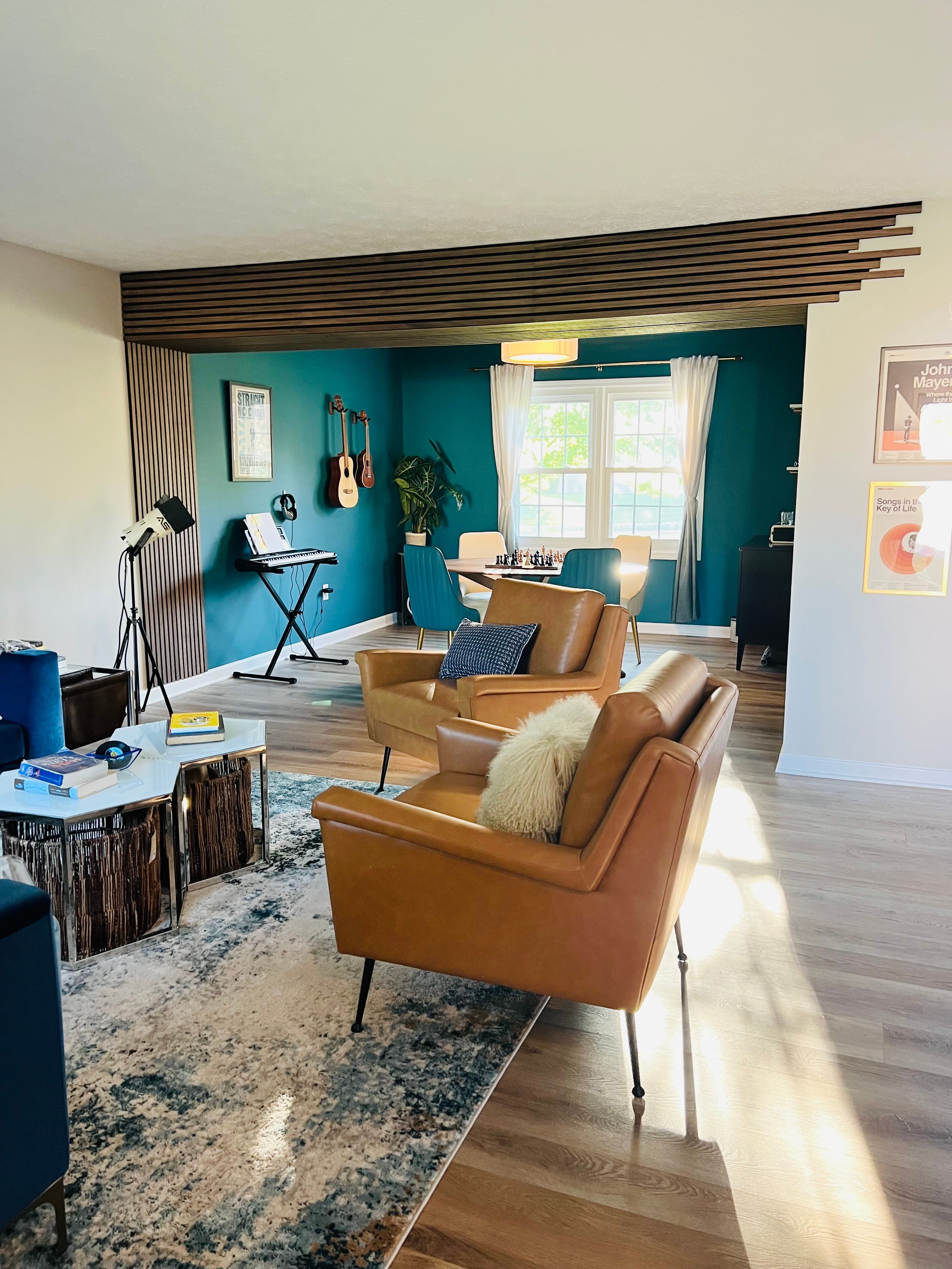 The living room after, camel leather chairs and a navy sofa on a patterned rug, opening onto the teal-walled music studio.