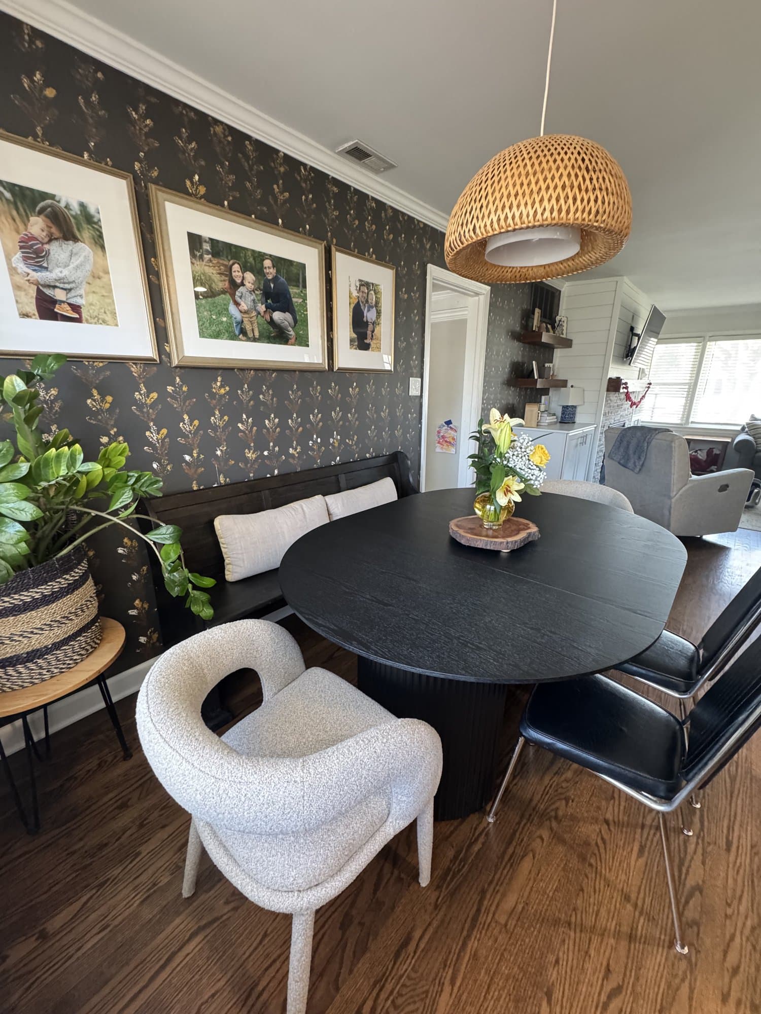Kitchen Nook after, a charcoal-and-gold botanical wallpaper wrapping the nook, layered with a framed gallery wall, a black pedestal table, and cane chairs.