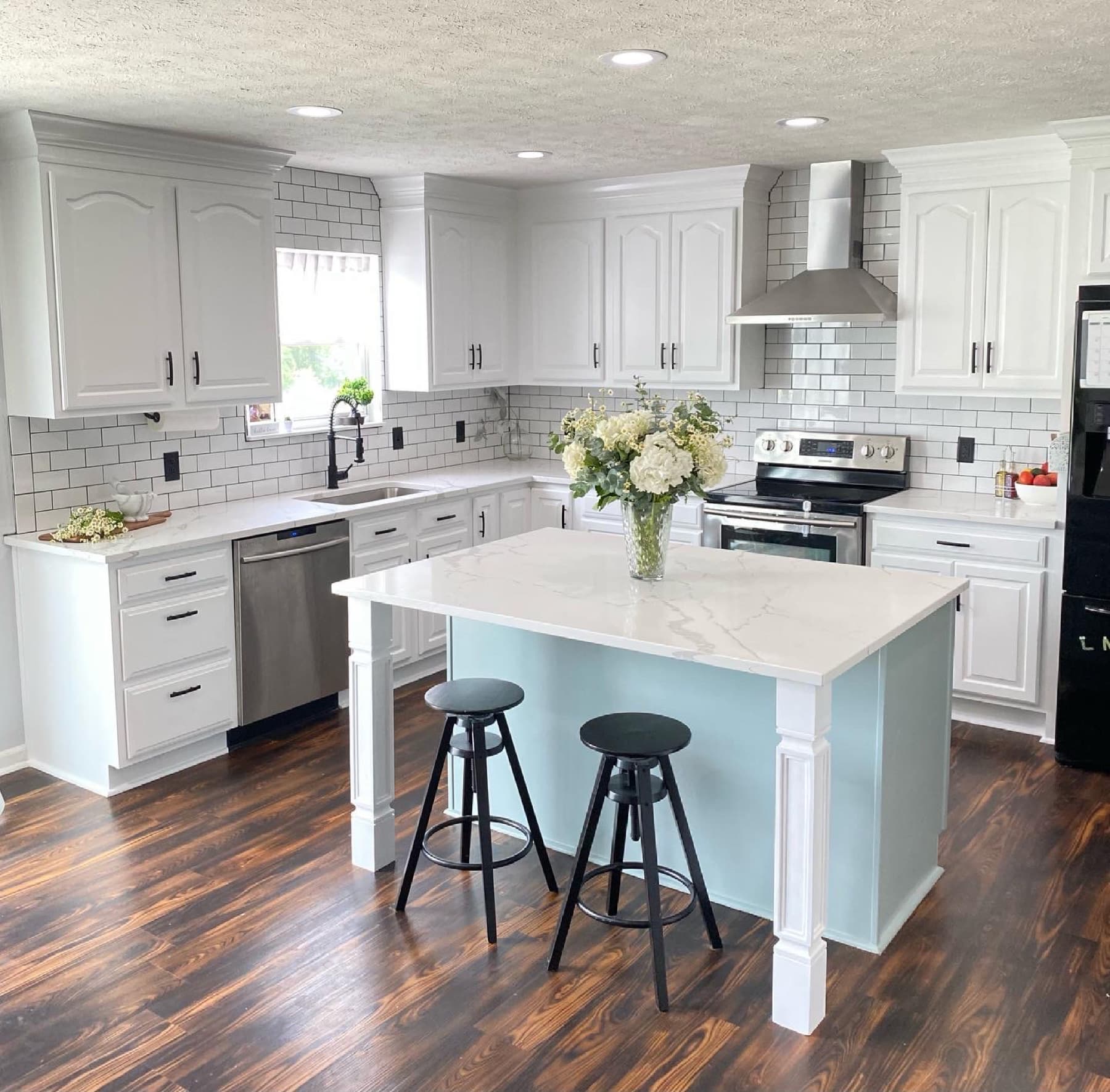After, a bright white kitchen with an island, range hood, and counter stools.
