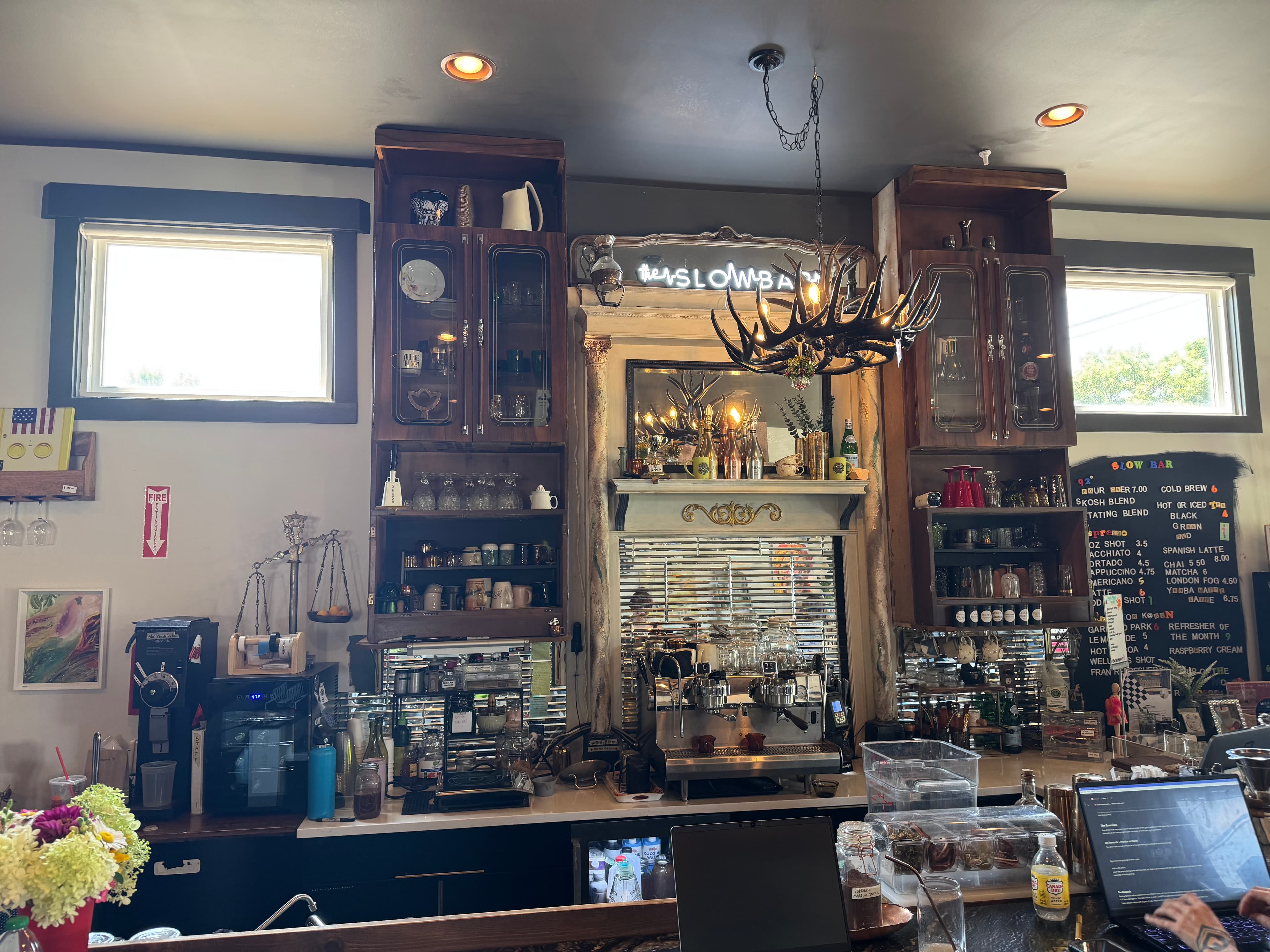 Skosh, the finished coffee bar with black-walnut cabinetry, brass fixtures, an antler chandelier, and a neon 'the Slow Bar' sign.