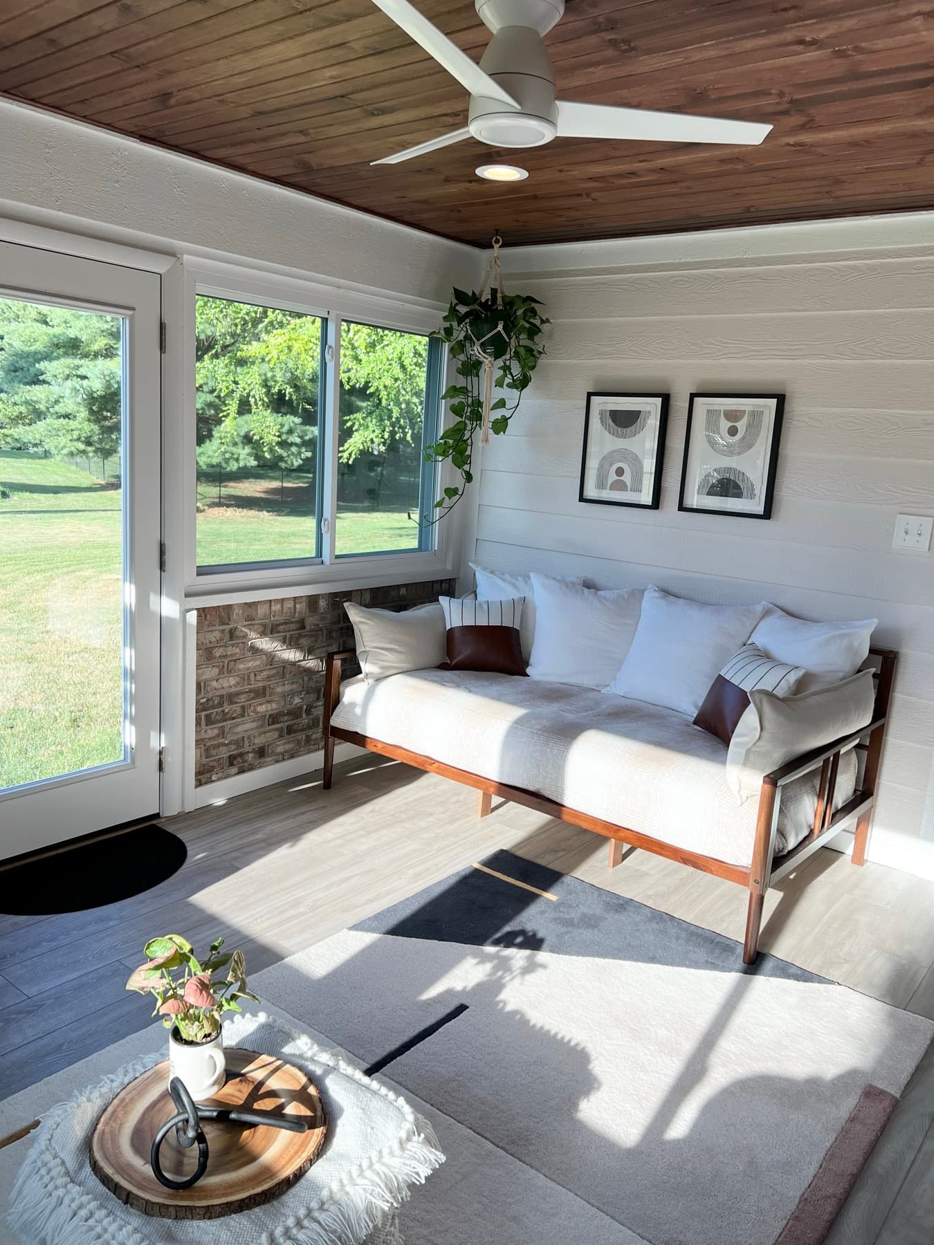 A bright sunroom with linen seating, a gallery wall, and greenery against the windows.